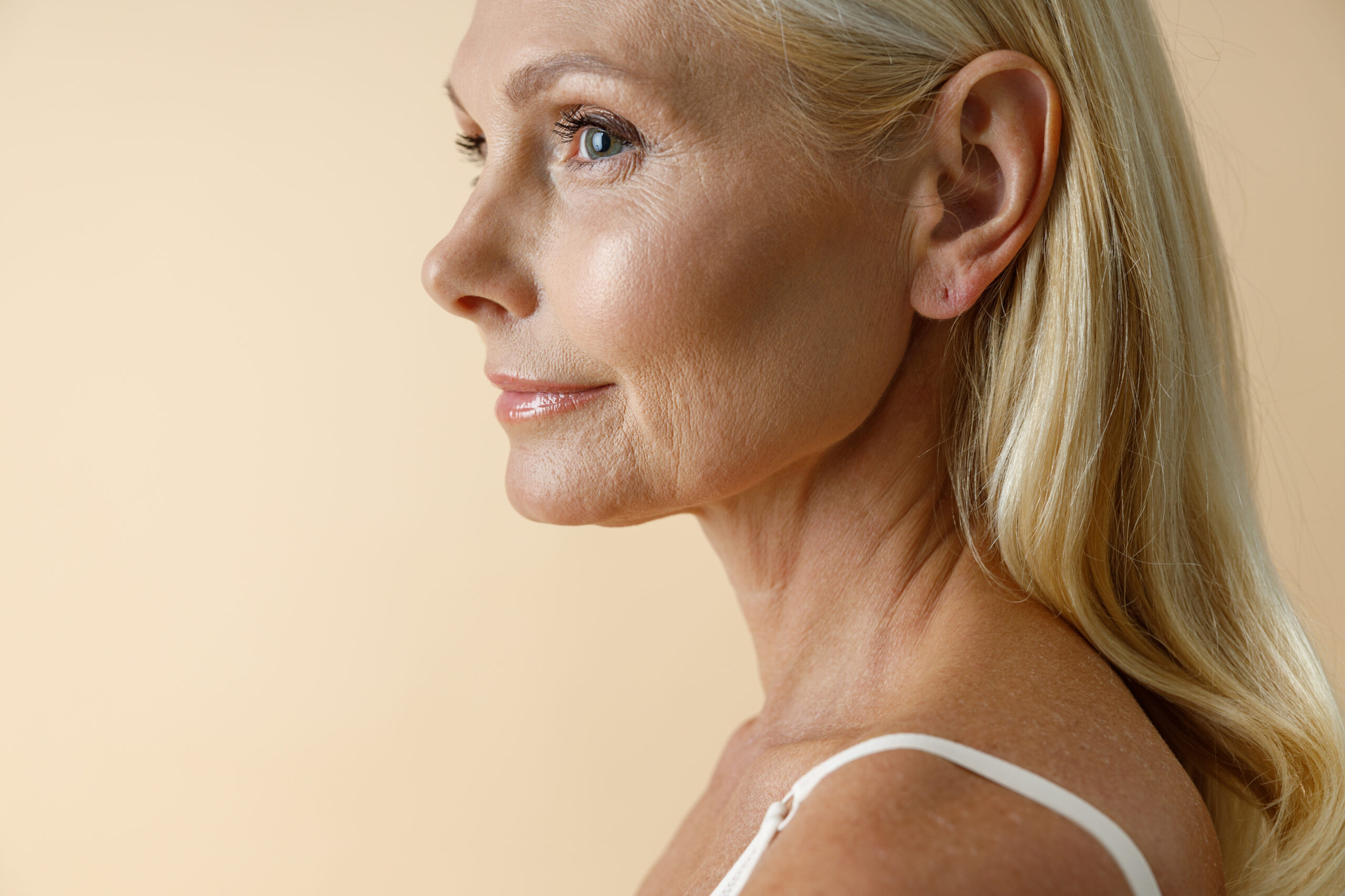 close up portrait mature blonde woman white underwear looking away posing isolated beige scaled